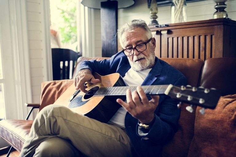 Elderly man playing an acoustic guitar at home, keeping his mind sharp and active
