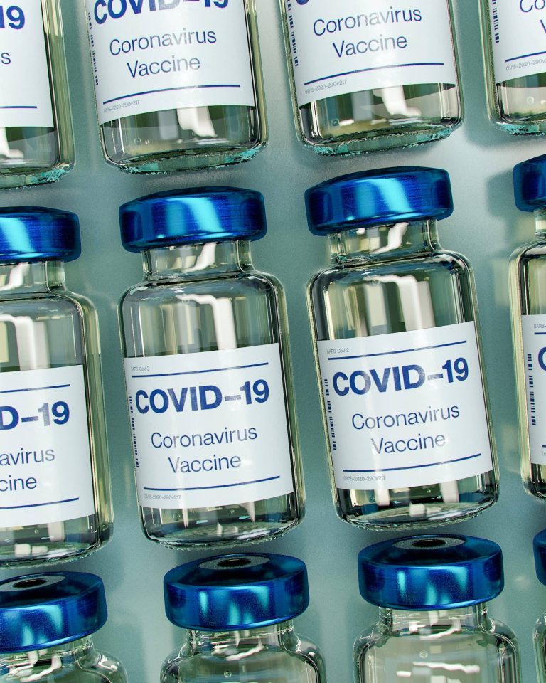 Gloved hands drawing a dose of COVID-19 vaccine into a syringe from a small glass vial