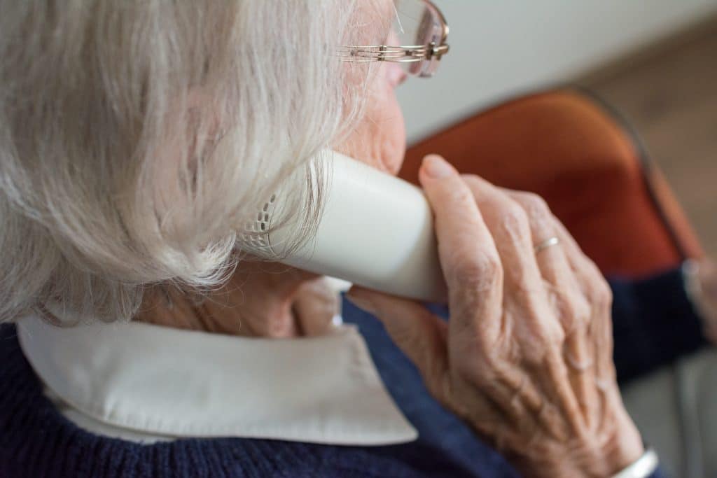 Elderly woman talking on a landline telephone at home, wary of a possible Medicare fraud call