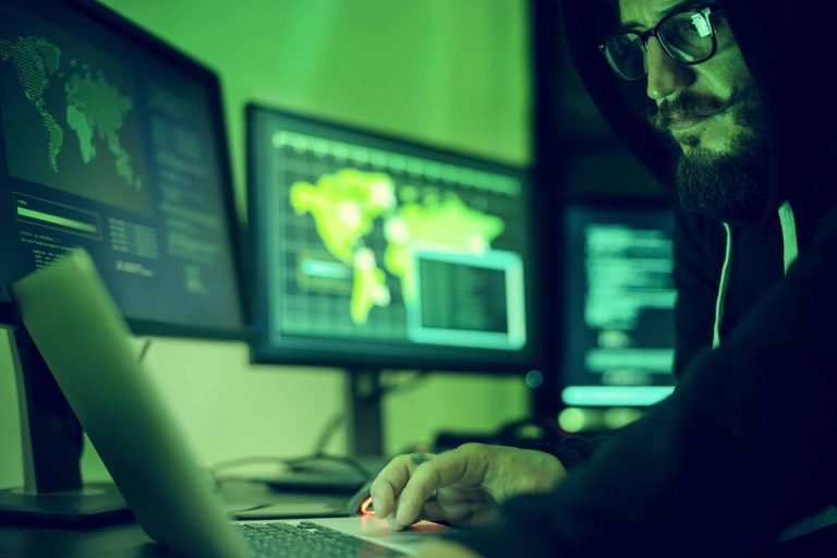 Hooded figure working at a laptop in the dark, illustrating identity theft and Medicare fraud