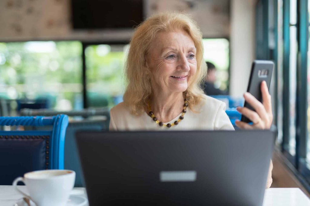 A smiling senior woman using her phone and laptop