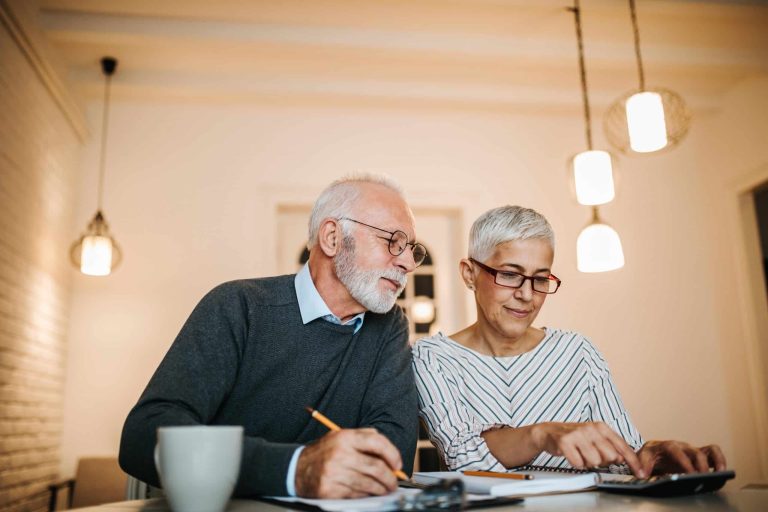 Older couple reviewing paperwork and a calculator with an advisor while making a financial plan