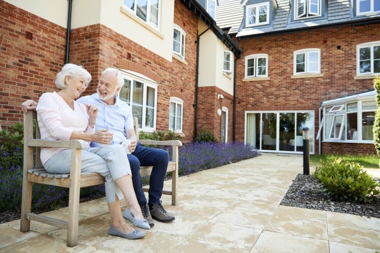 Retired couple sitting together on a bench with hot drinks at an assisted living facility