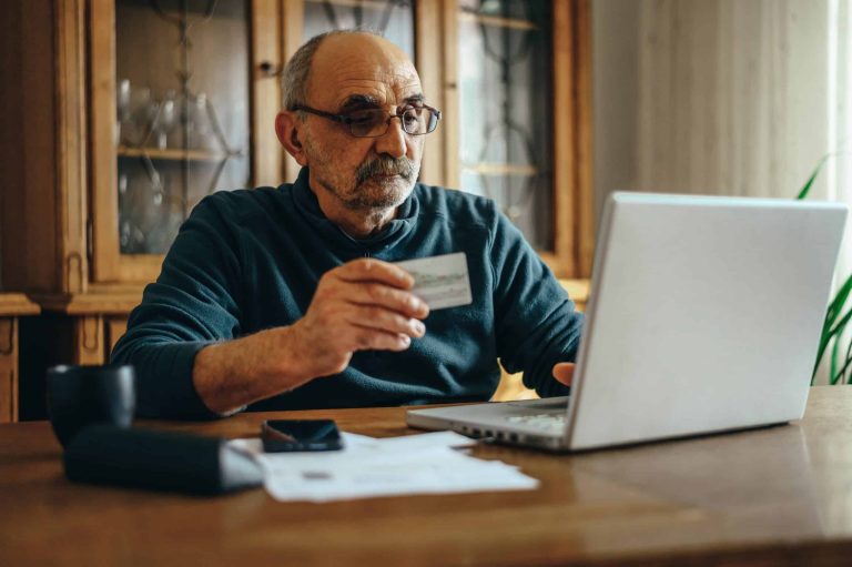 Senior man entering card details on a laptop to pay online, a common target for Medicare scams
